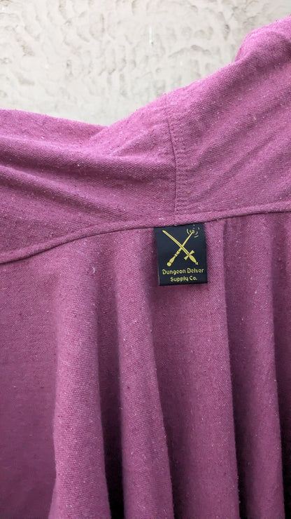 Close-up of a dusty purple or mauve knit garment, likely a dress, featuring a black sewn-in label with gold text and logo that reads 'Dungeon Delver Supply Co.'.
